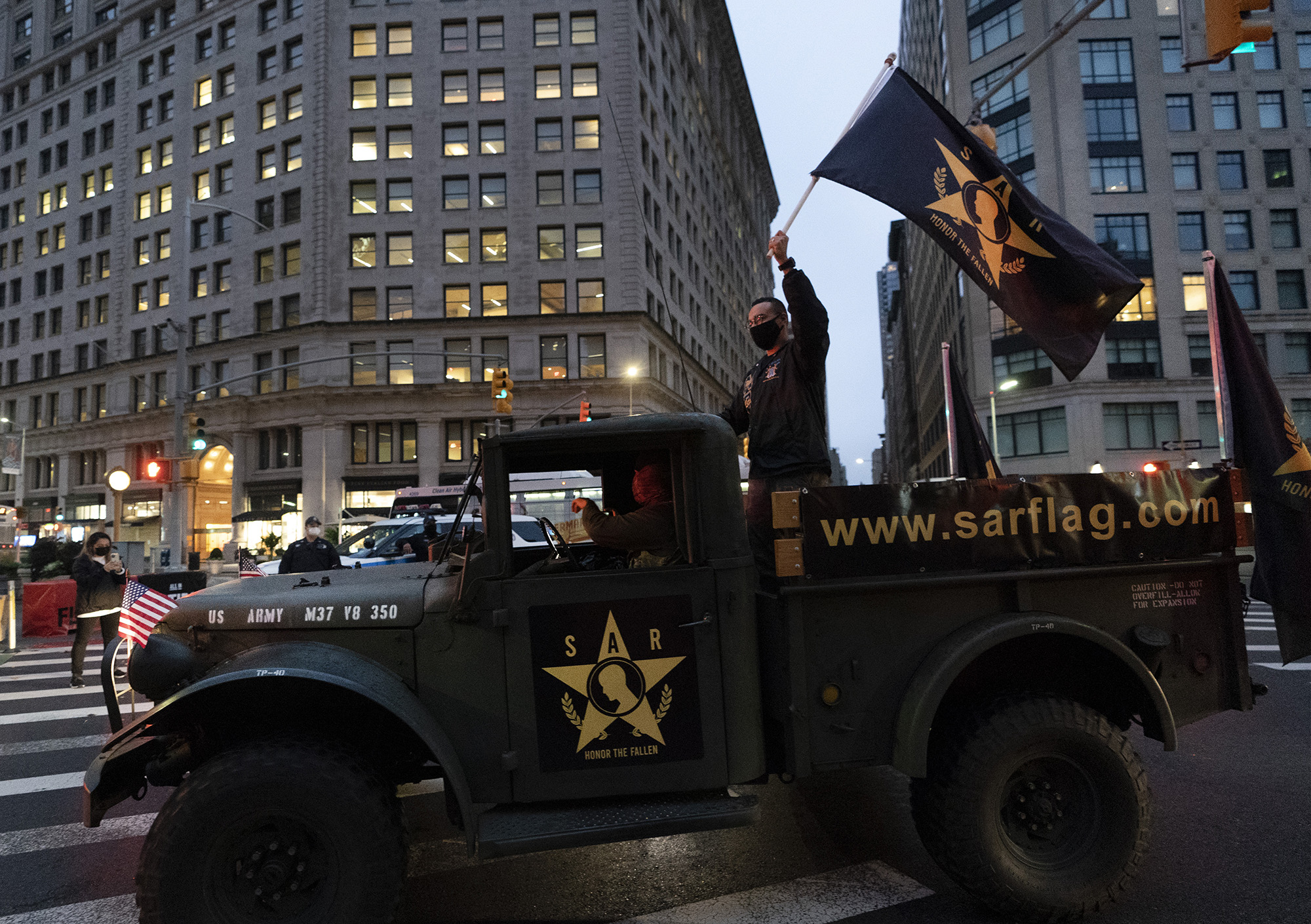 A man waves a flag as he stands in the back of a military vehicle during a Veterans Day parade, Wednesday, Nov. 11, 2020, in New York.